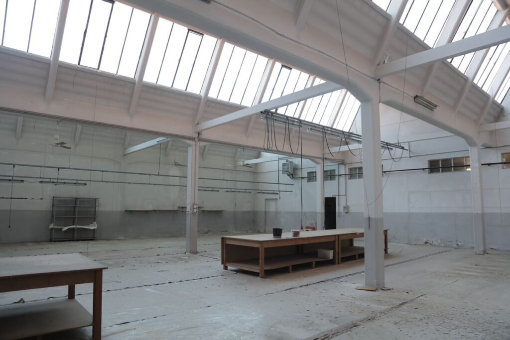Nave industrial vacía con piso de hormigón, estructura metálica y lucarnas en el techo